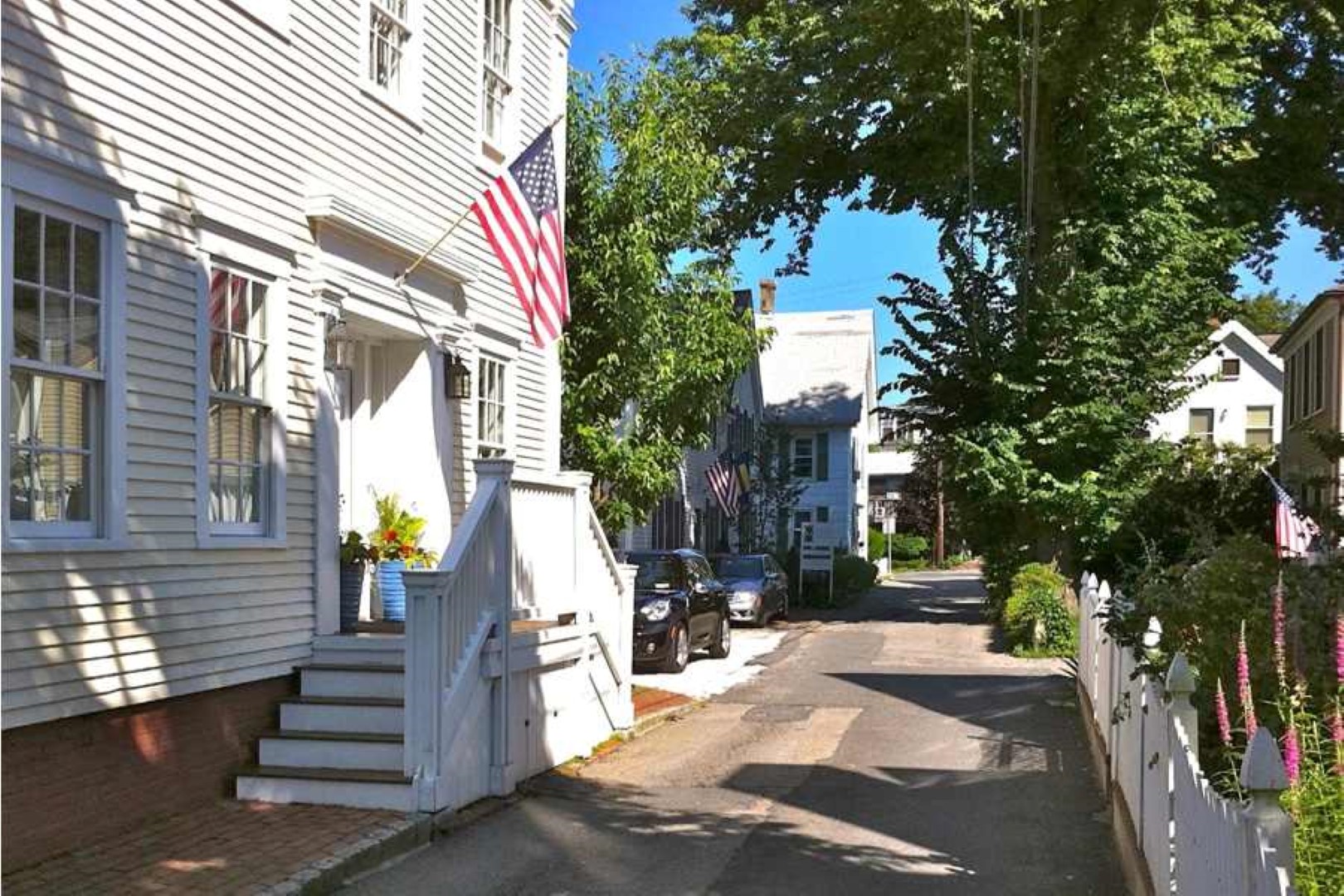 narrow street with Benchmark Inn to the left, front steps and front door. street lined with gardens and trees